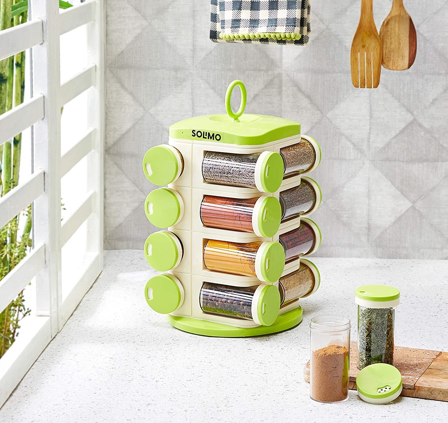 The spice rack kept on a kitchen counter. The jars have green lids and contain different spices.