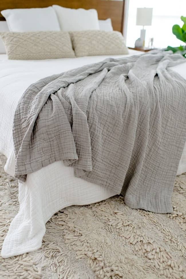 gray oversizes muslin comfort blanket on a bed that has a white comforter on it