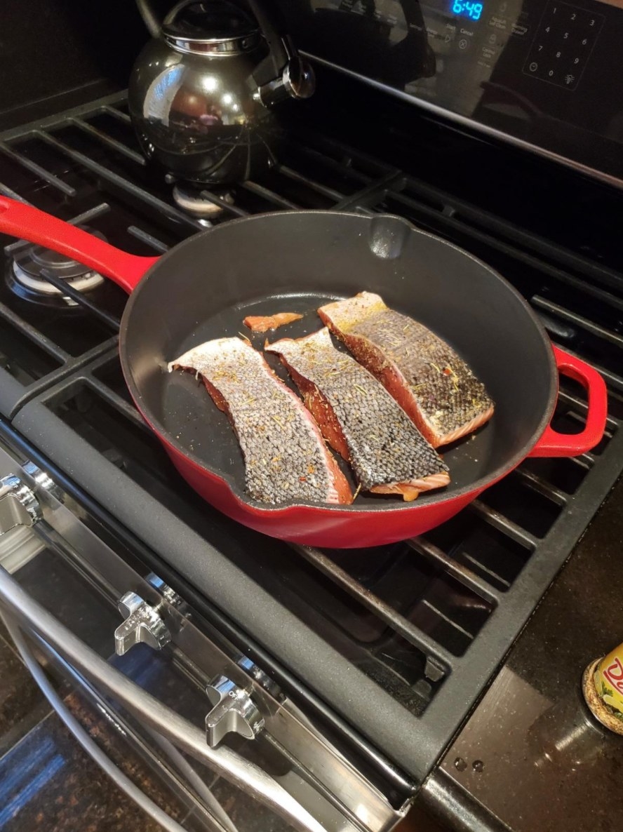 The enameled cast-iron skillet in red cooking salmon 