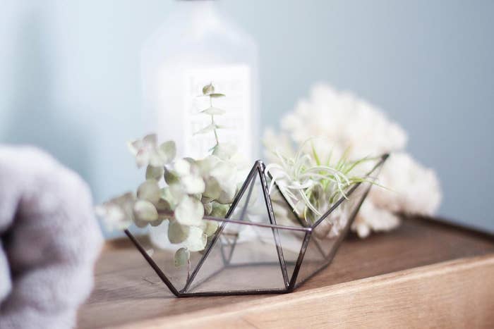 A glass origami boat on a desk with flowers in it 