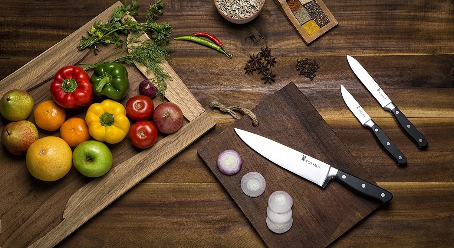 The knives are kept on a wooden chopping board. Vegetables and spices are kept around them.
