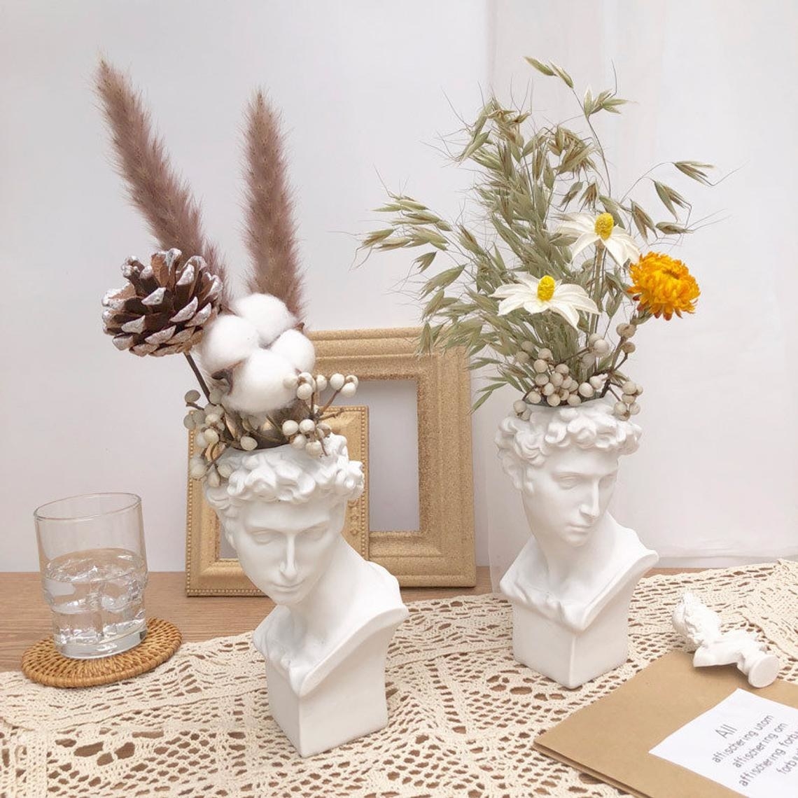 two bust vases on a table with flower arrangements in each