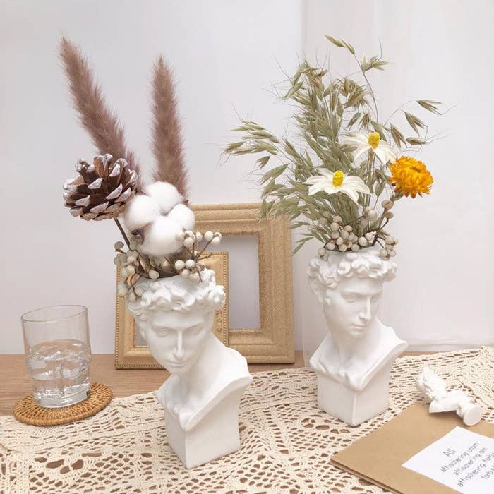 two bust vases on a table with flower arrangements in each 