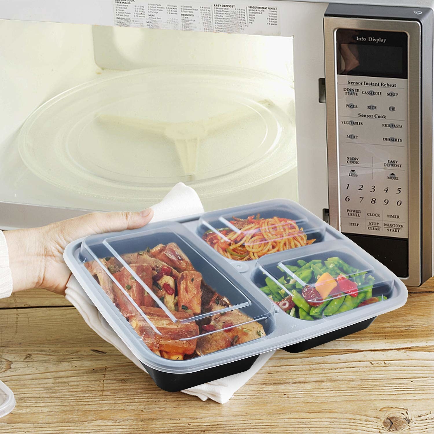 Meat, pasta, and salad stored in the three compartments of the bento box. A person is about to microwave it.