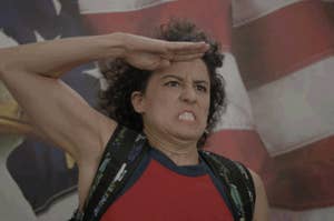 Ilana from Broad City giving a spirited salute in front of an American Flag