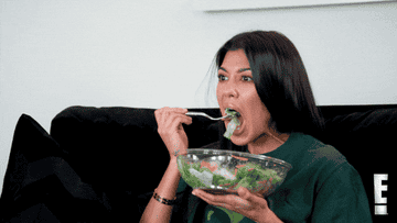 Kourtney Kardashian eyeballing someone offscreen while eating a salad. 