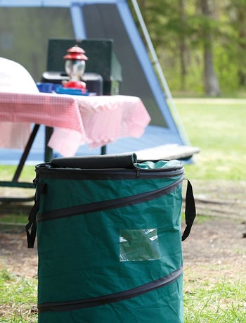 the green pop up trash can sitting in front of a picnic bench