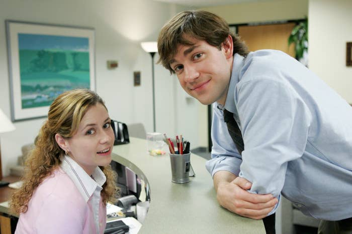 Pam smiles while Jim leans over on her desk