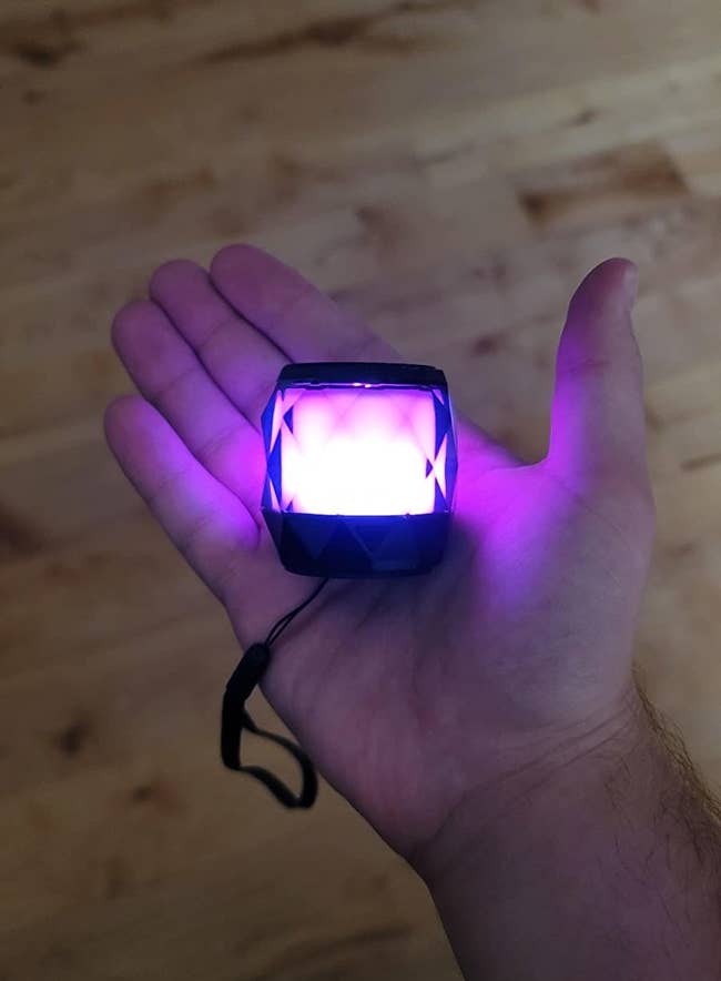 image of a lit up LFS portable bluetooth speaker in a reviewer's hand