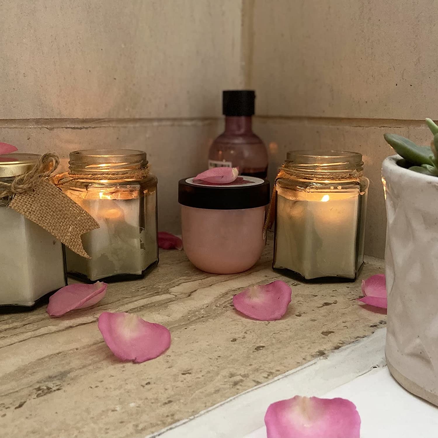 Lit glass jar candles with rose petals scattered about 