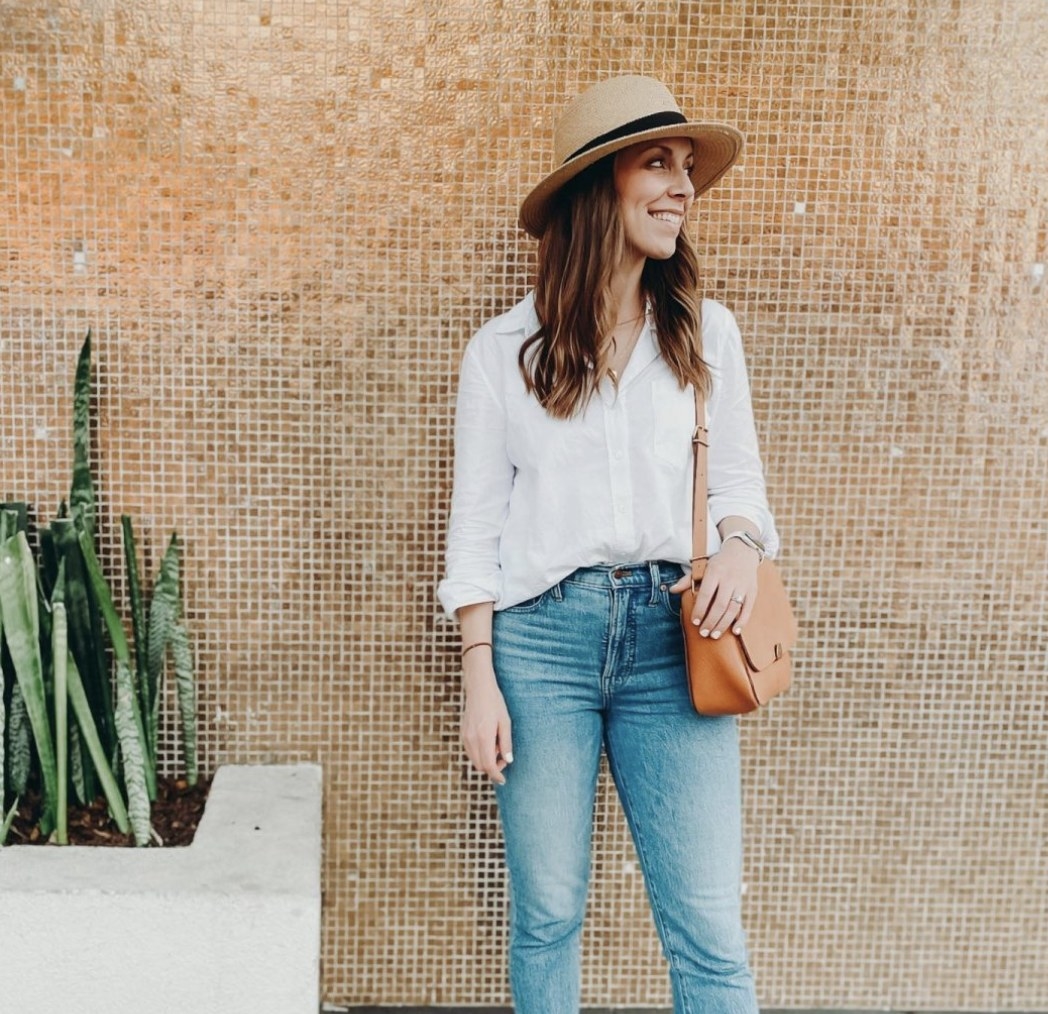 A person wearing a straw hat, white top, and denim jeans