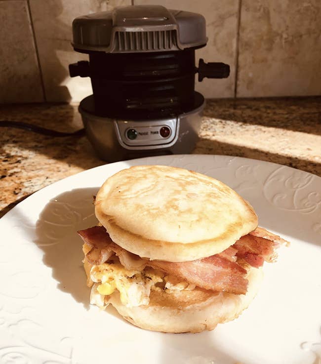 Egg bacon cheese sandwich sitting in front of the metal cylinder shaped cooker 