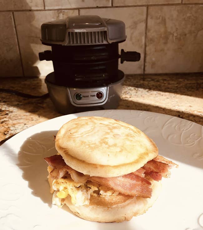 Egg bacon cheese sandwich sitting in front of the metal cylinder shaped cooker 