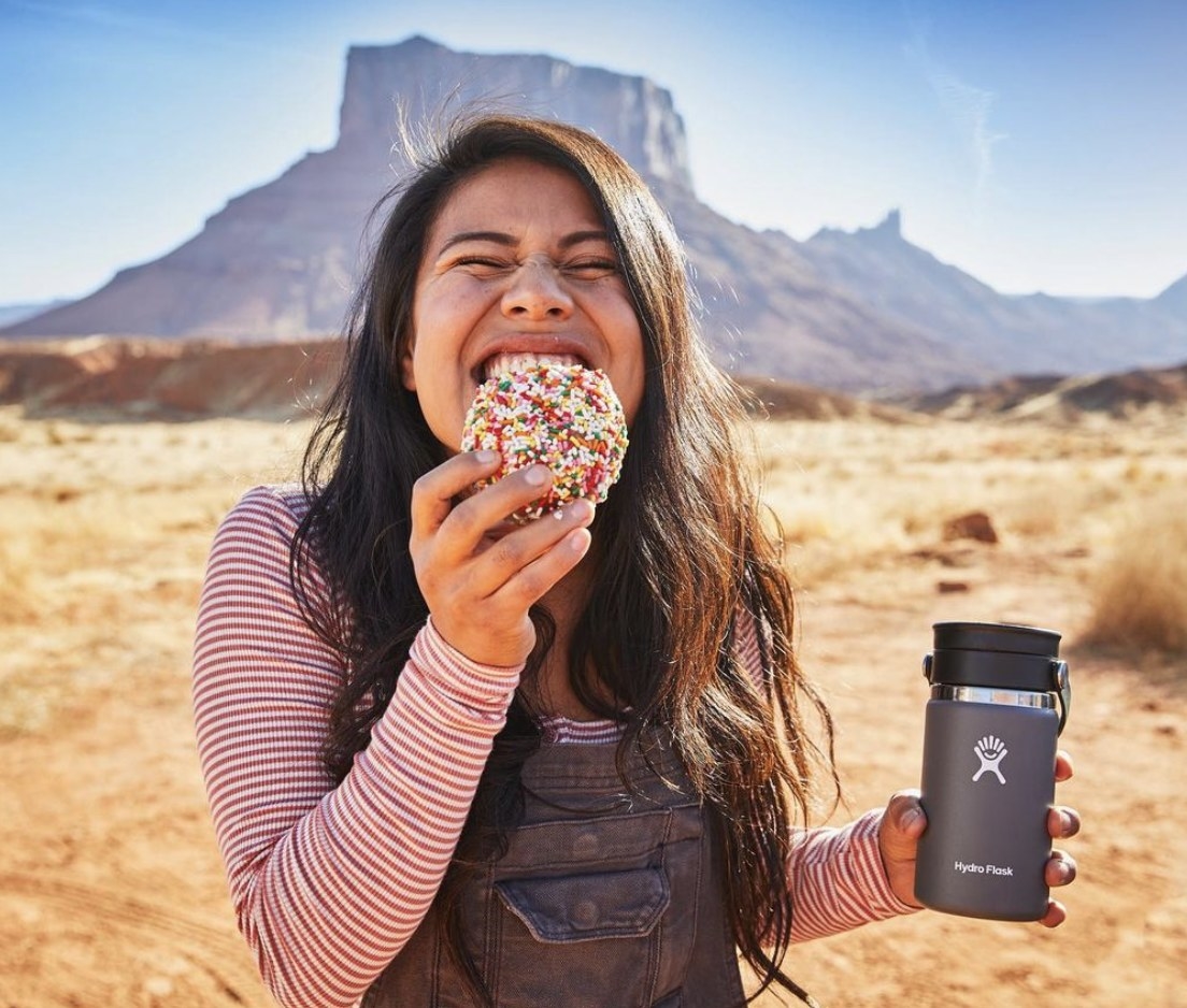 A person eating a donut and holding a grey Hydroflask
