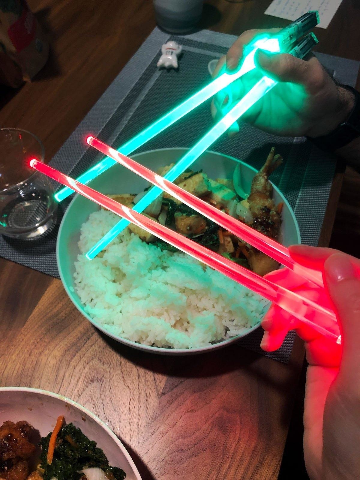 Reviewers holding light-up lightsaber chopsticks 