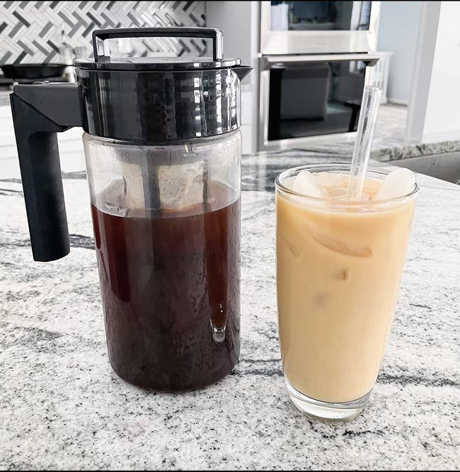 A pitcher of cold brew coffee next to a cup of creamed cold brew 