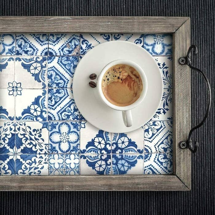 A tea cup sitting on a wooden tray with a wallpapered backing