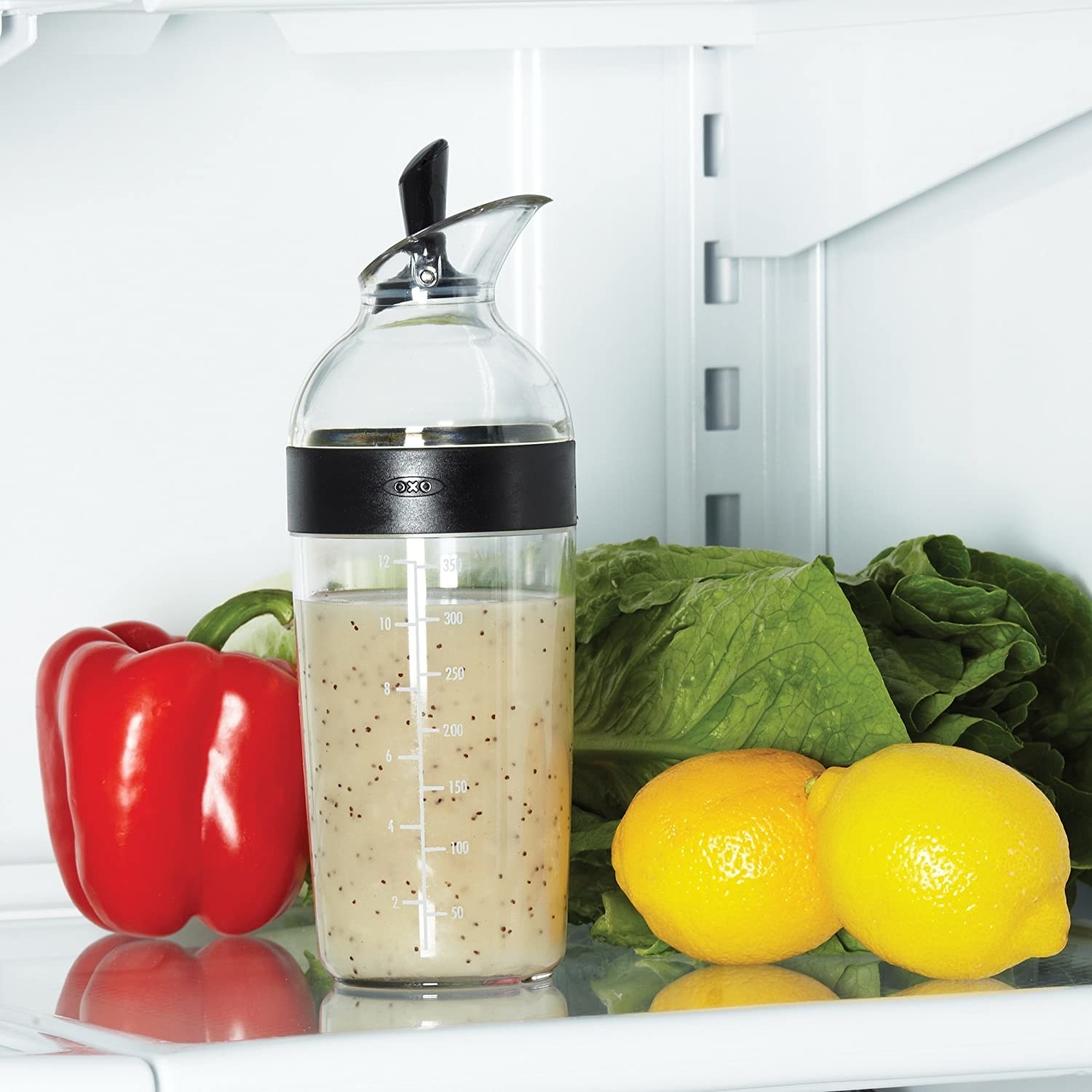 A bottle of salad dressing a fridge shelf with bell peppers, lettuce, and lemons