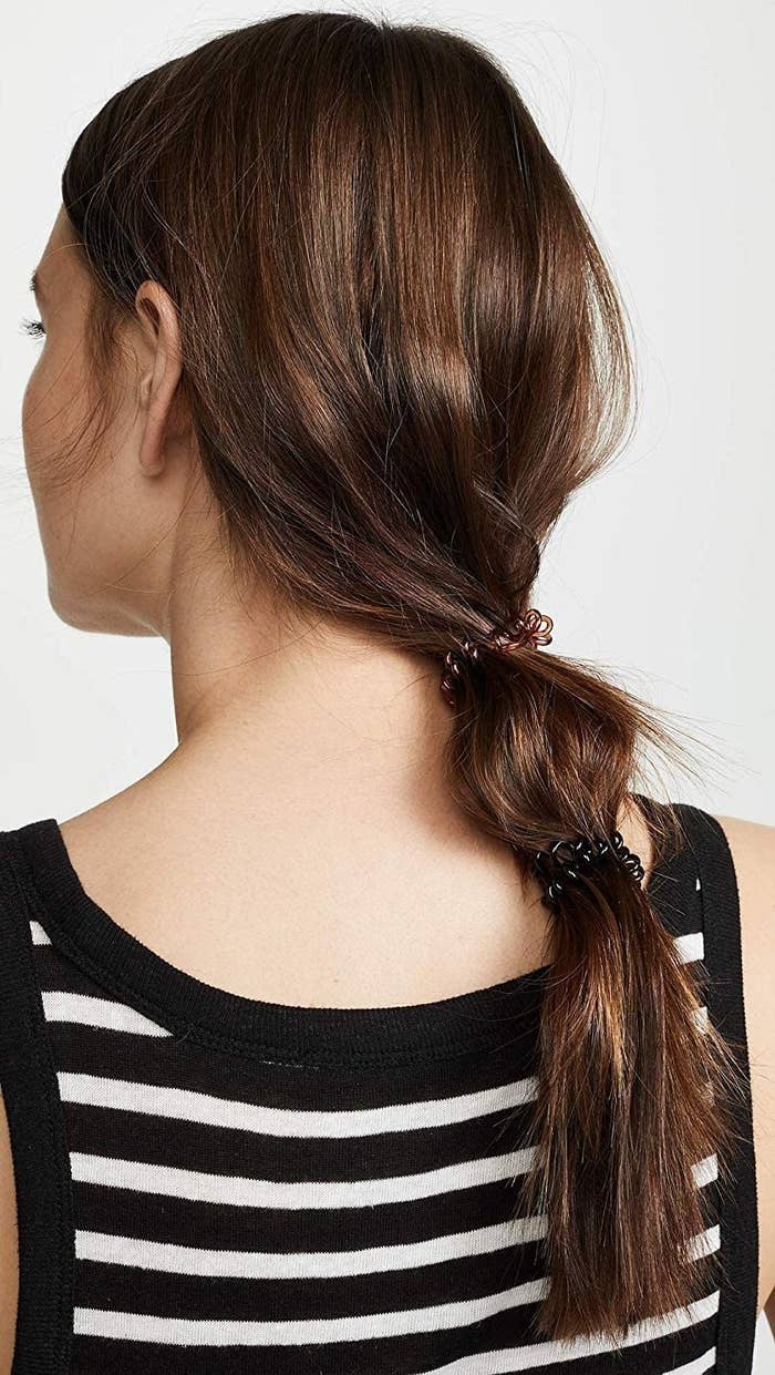 A person with their long hair in a ponytail using coiled hair ties