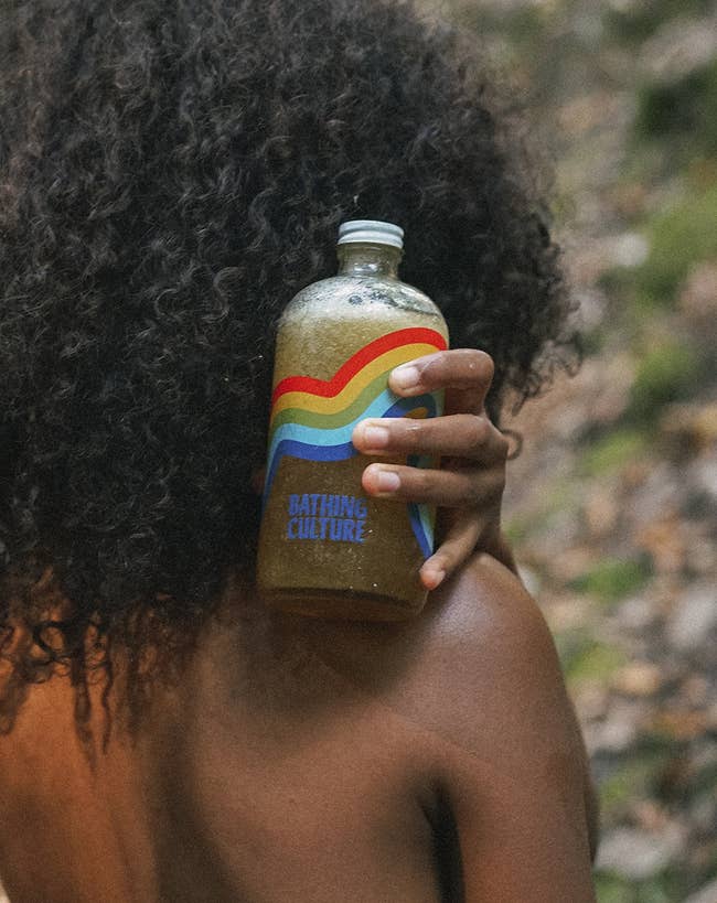 model holding a glass bottle of body wash with a rainbow design on the front