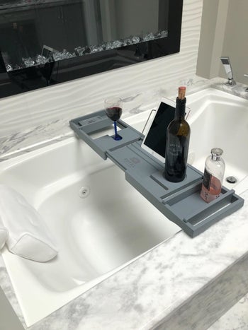 reviewer photo of a bath caddy with a wine bottle and accessories on it 