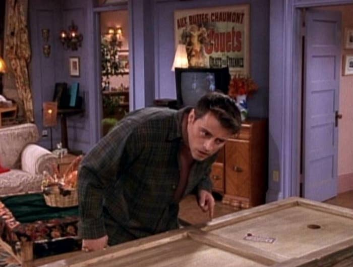 Joey leans his ear down to listen to Chandler who is laying in a long wooden box.