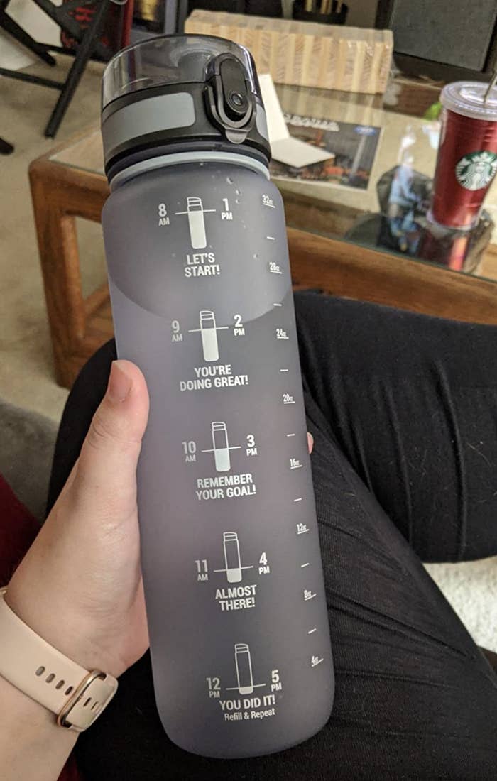 Reviewer holding gray water bottle with white time markings on them 