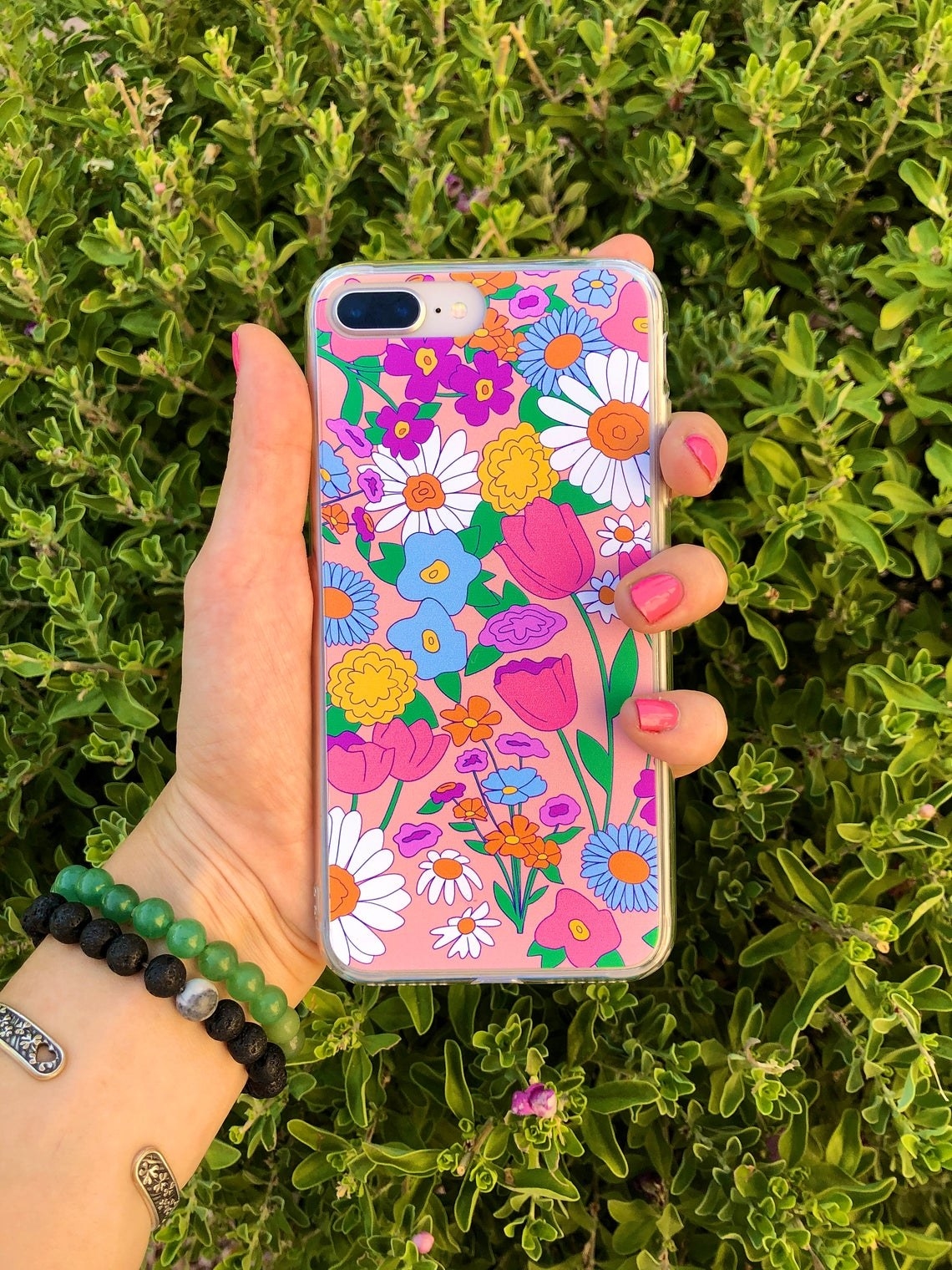 a person holding a bright, floral phone case over grass 