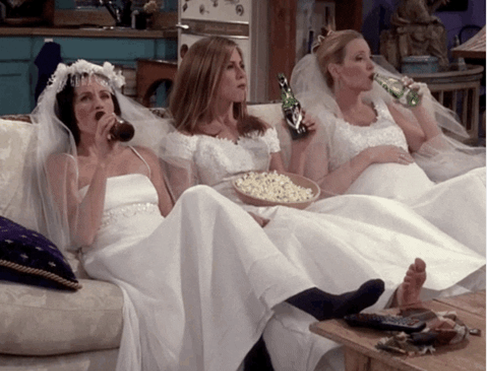 Monica, Rachel, and Phoebe all wearing wedding dresses and kicking back on the couch