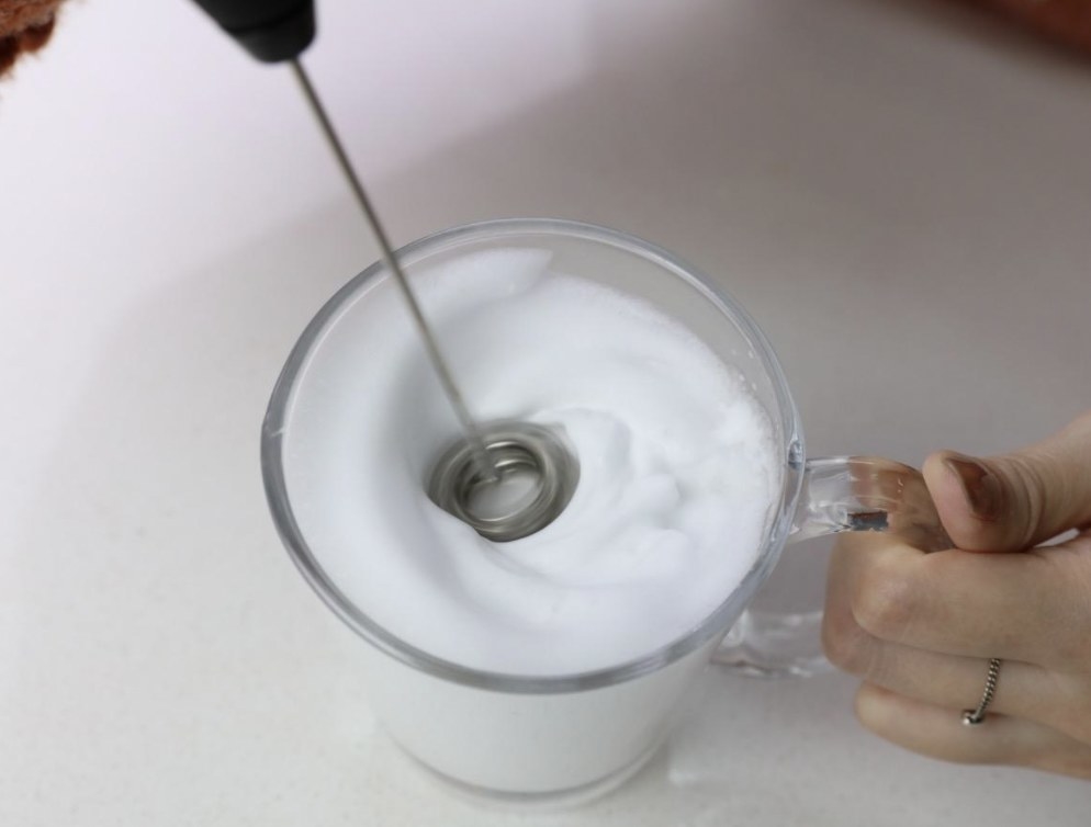 a person using a milk frother to froth milk