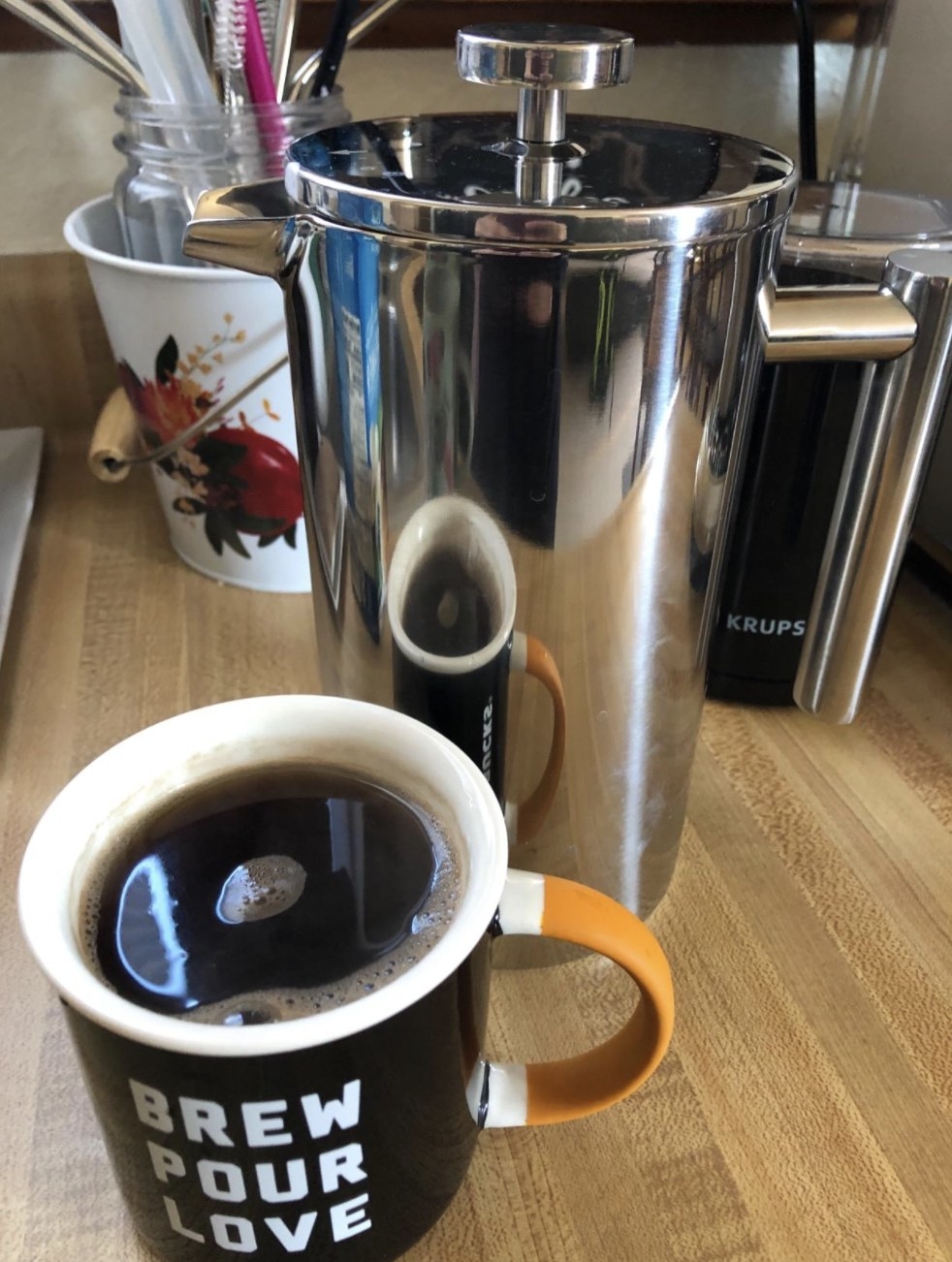 a silver french press with a black cup of coffee in front of it 