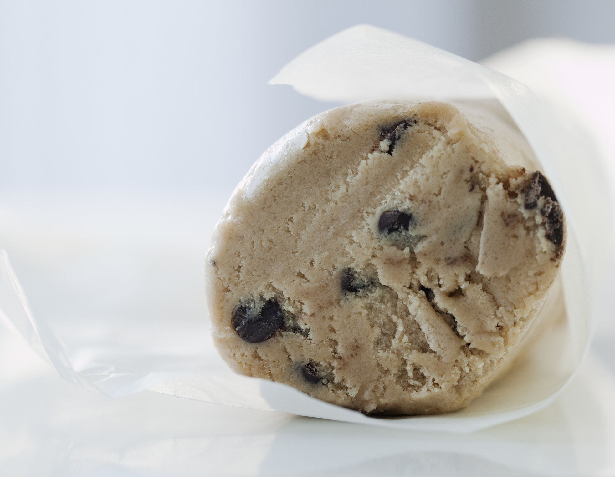 A roll of chocolate chip cookie dough in wax paper.