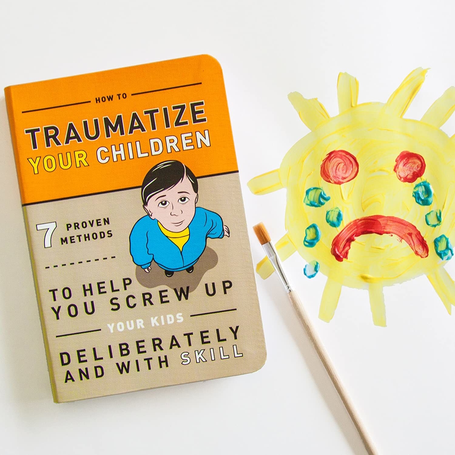 The cover of How to Traumatize Your Children next to a child-like painting of a sad sun