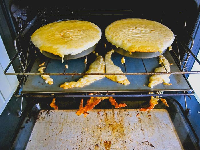 Two uncooked cakes in the oven with dough spilled all over the place