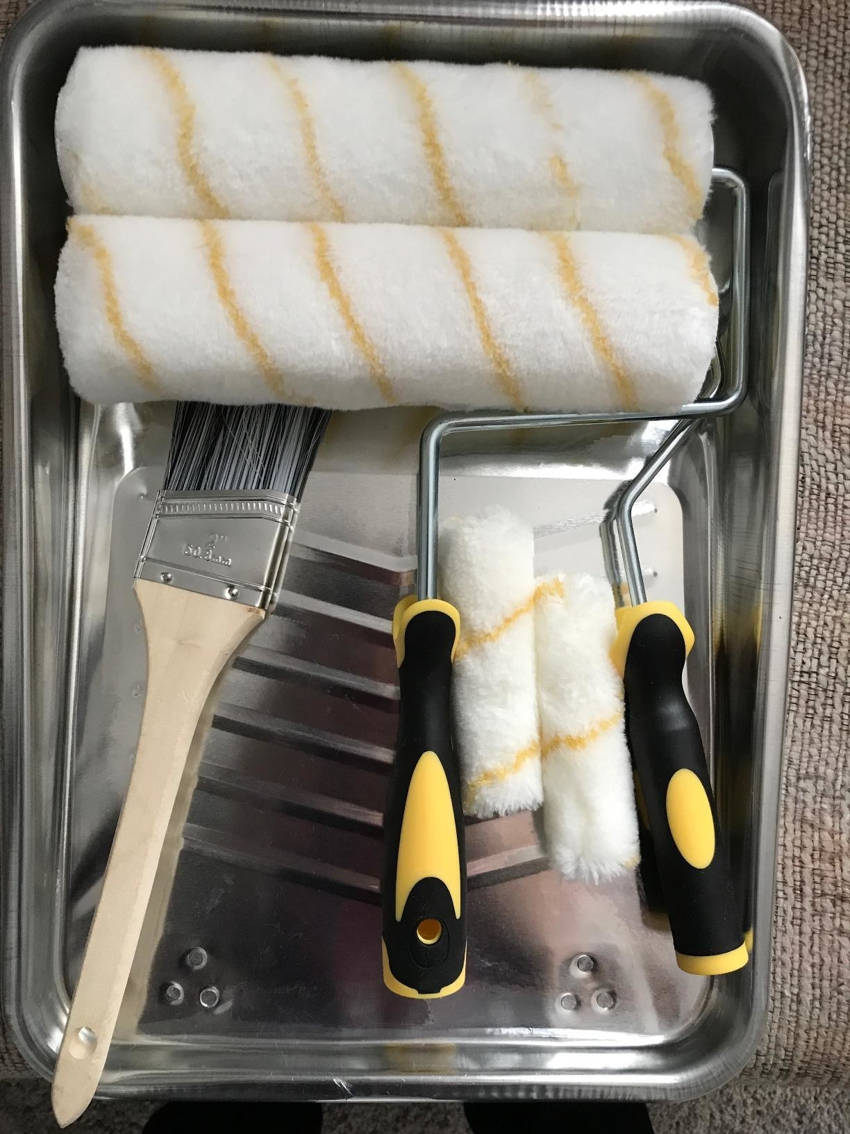 a reviewer photo of a silver paint tray filled with two large and two small roller brushes and a wooden paint brush