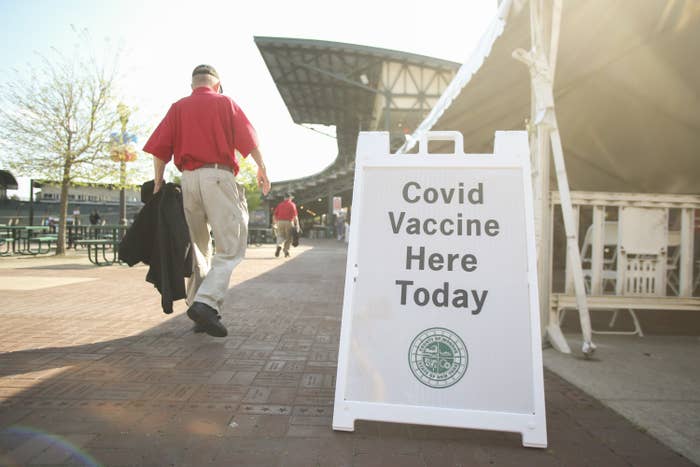 A man walks by a sign that reads &quot;Covid Vaccine Here Today&quot;