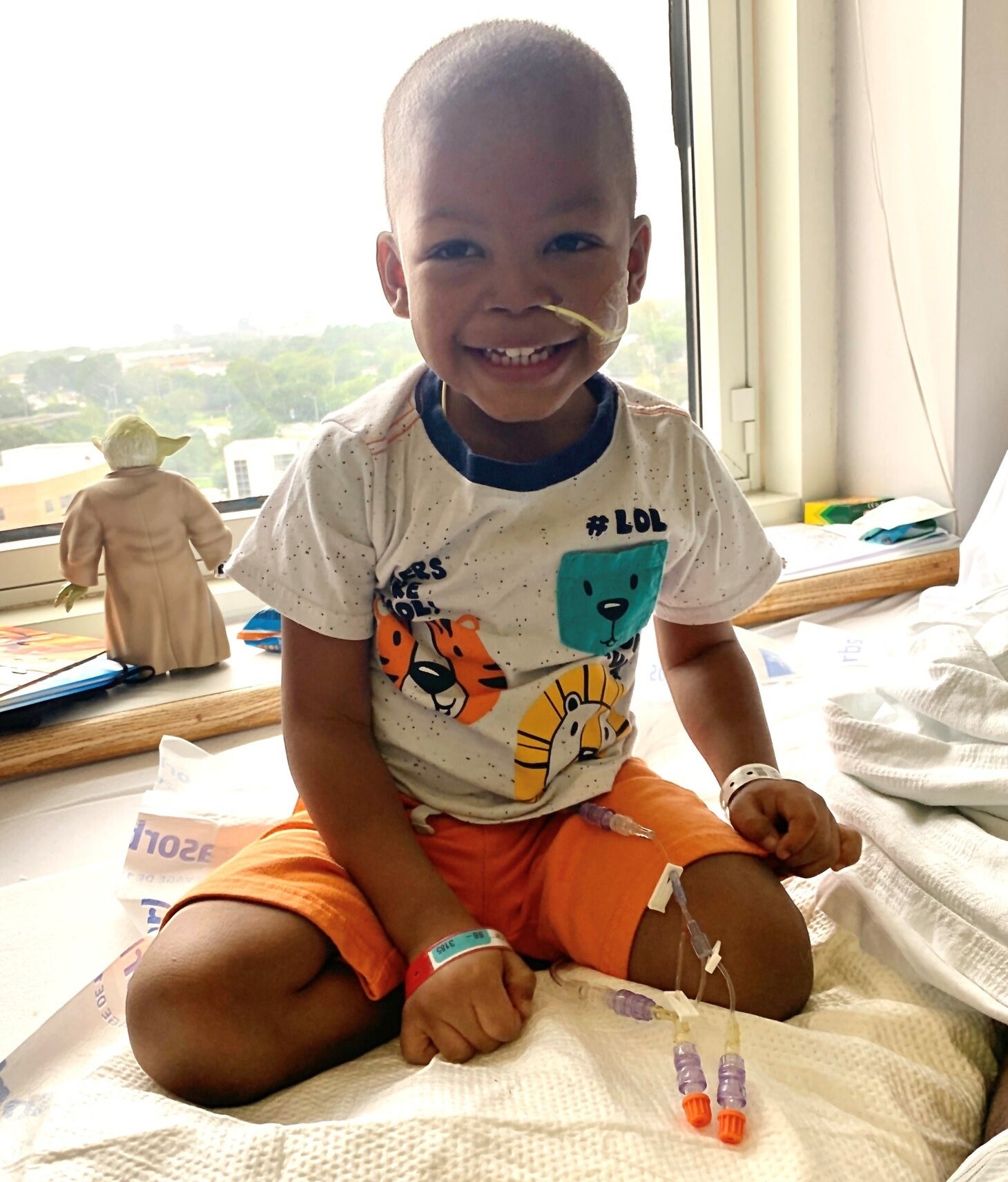 A young boy sits upright in a hospital bed, smiling
