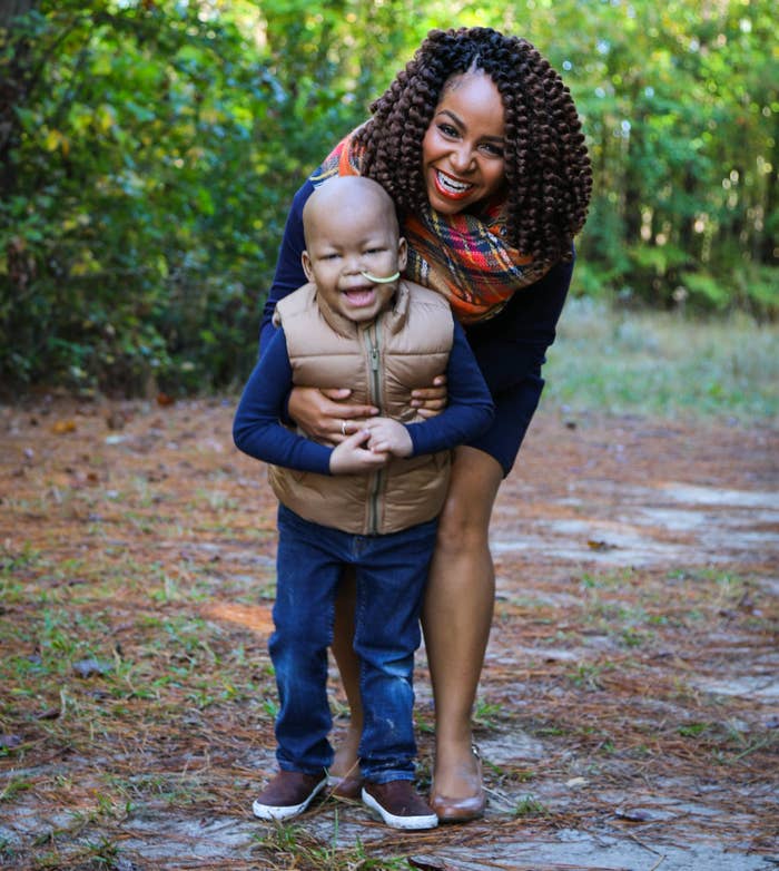 A woman smiles and hugs her son with a tube in his nose while standing in the woods