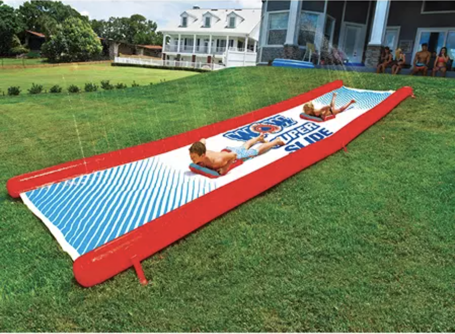 Kids play on a water slide in a yard.