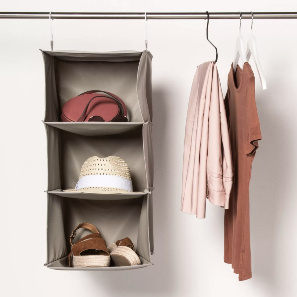 Gray three-shelf hanging organizer with a patterned fedora and folded towels