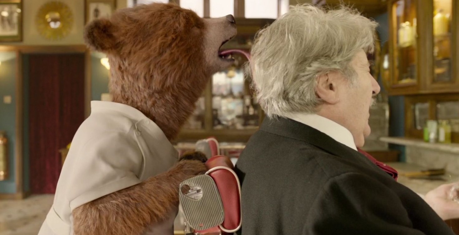 Paddington wears a white barber uniform and licks the back of the head of an old man in a barber&#x27;s chair who is cringing