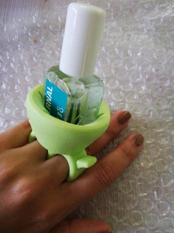 a reviewer photo of someone wearing the nail polish holder with a bottle of nail polish inside