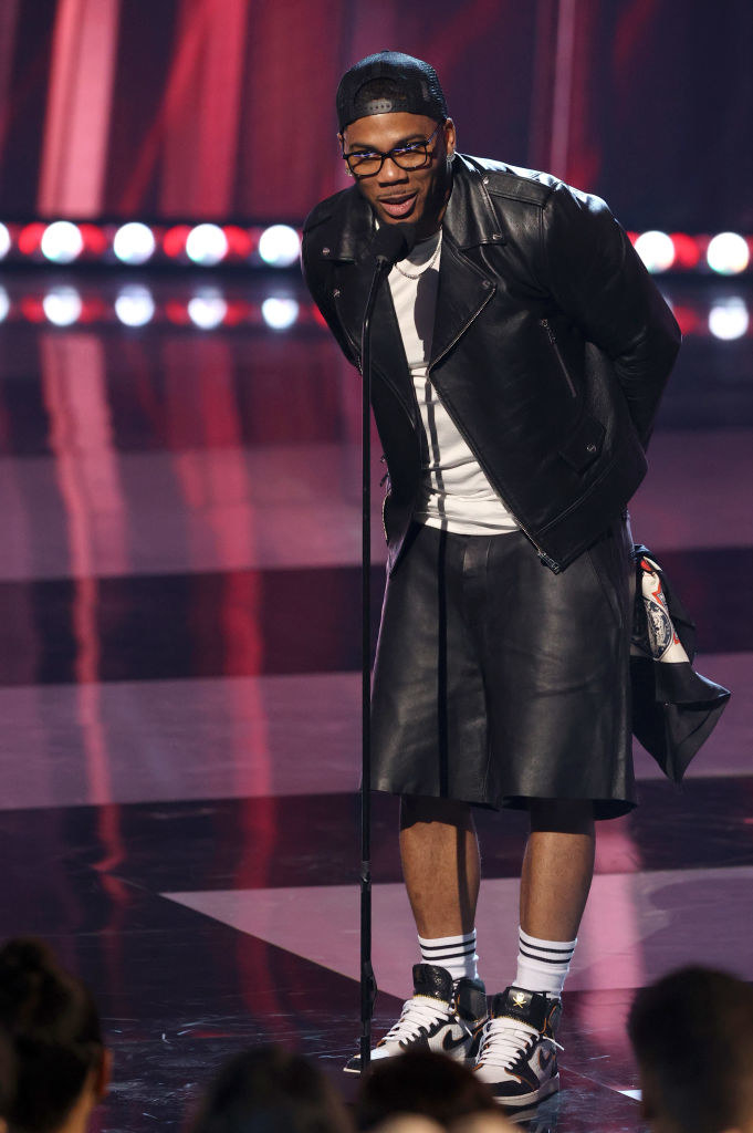 Nelly speaks onstage at the 2021 iHeartRadio Music Awards in leather shorts, a tee, and a leather jacket