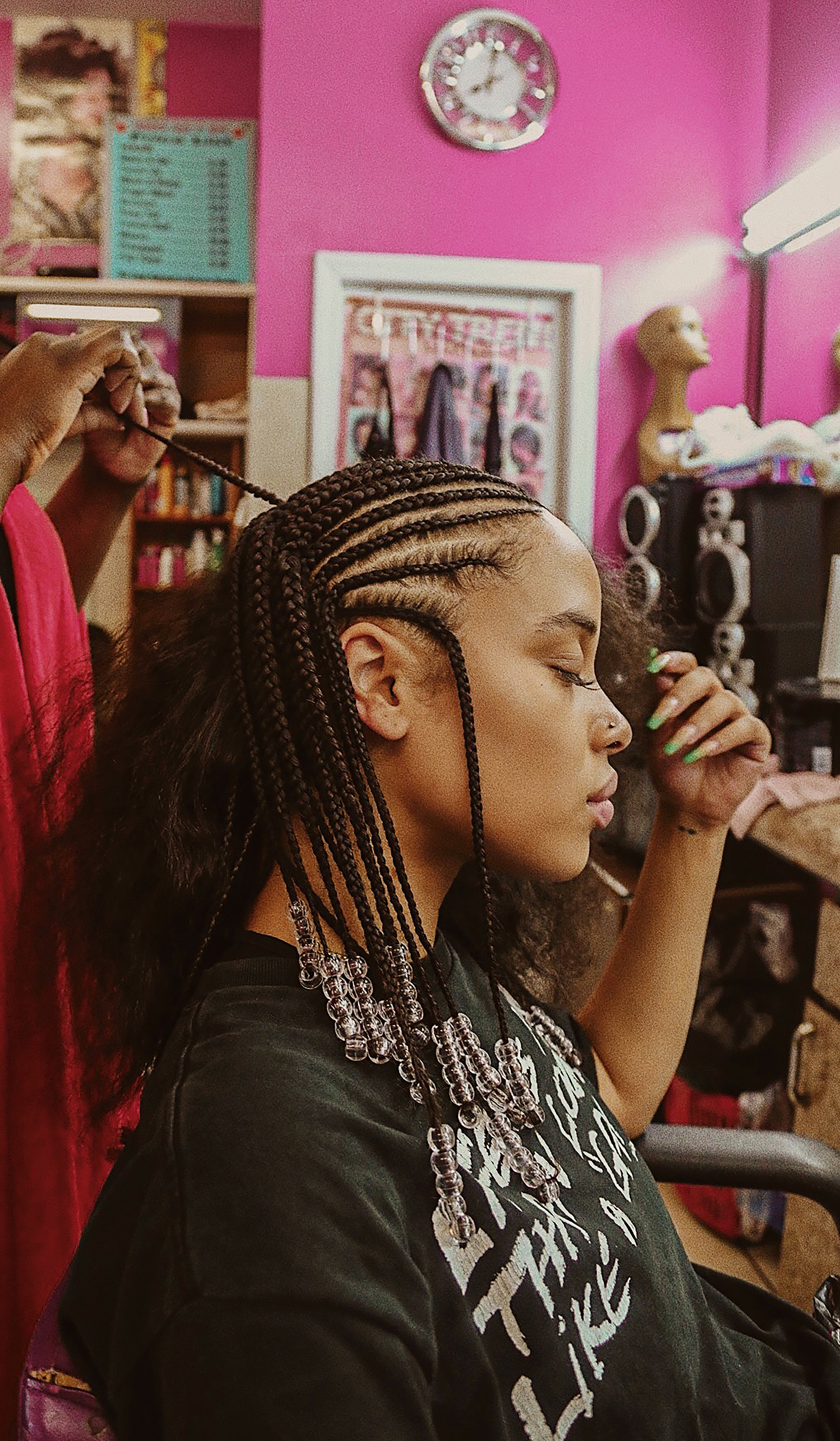 A woman sits while a hairdresser braids her hair