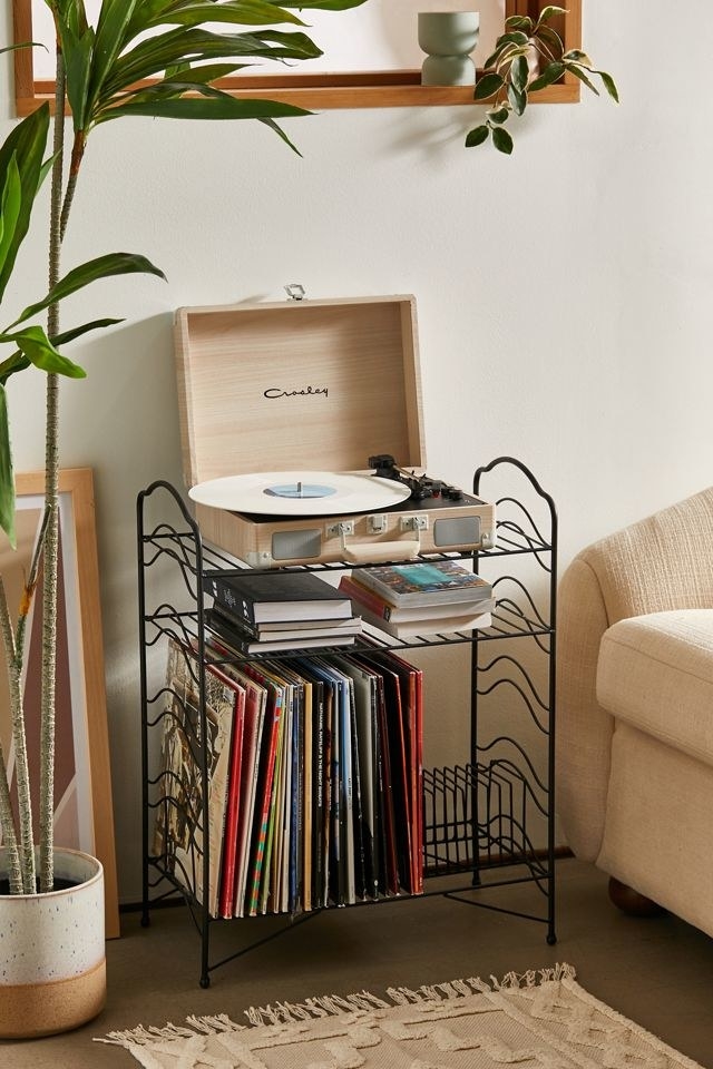 A black storage shelf with a record player on top and several vinyls on the bottom
