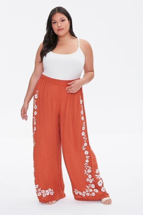 Model wearing orange pants with white embroidered flowers