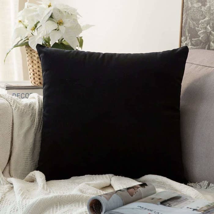 Black velvet cushion cover on a cushion. It&#x27;s placed on a sofa.