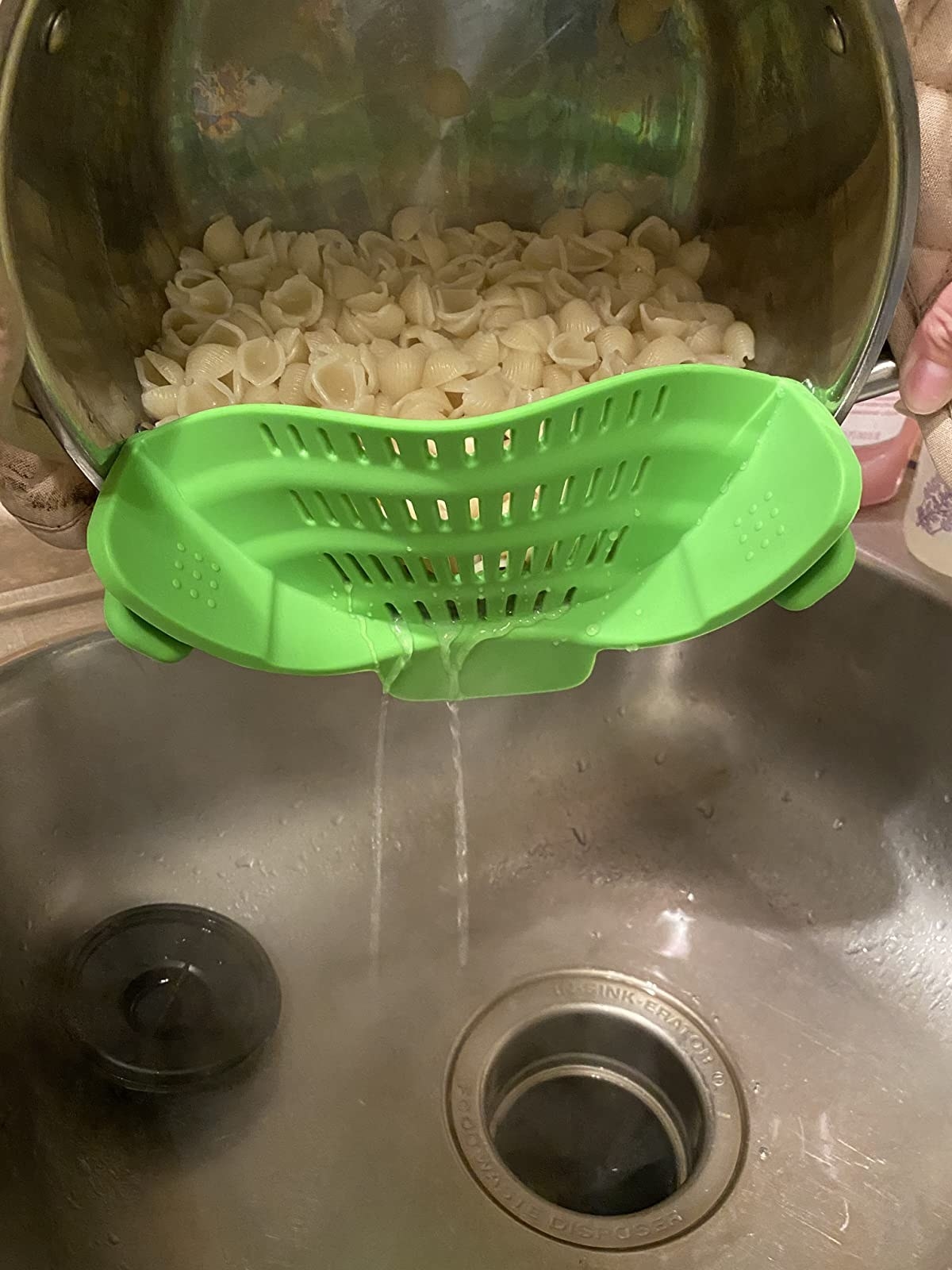 The colander clipped to the edge of a pot, draining water into a sink