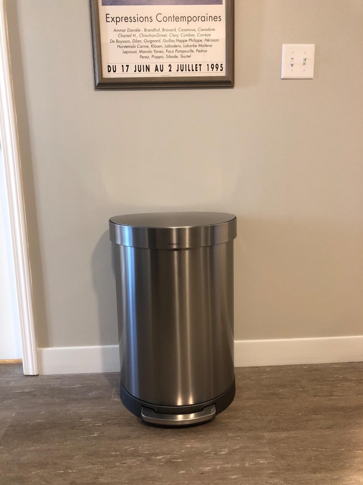 The trash can up against a wall with a stainless steel finish and pedal at the bottom