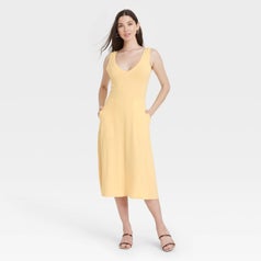 Model wearing yellow dress with two side pockets, goes past the knee
